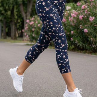 Ženske tamnoplave capri tajice sa sitnim cvjetnim uzorkom uparene s bijelim sportskim tenisicama na otvorenom.
